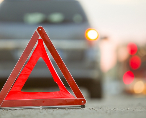 Red emergency triangle stop sign and broken car on a city street